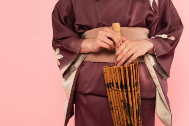 Cropped view of woman in kimono holding japanese umbrella isolated on pink  clipart