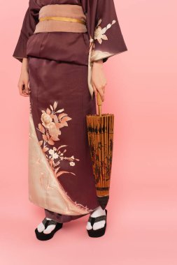 Japon kıyafetleri ve pembe arka planda şemsiye tutan kadın görüntüsü.