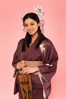 Şemsiyeli gülümseyen Japon kadın pembe üzerine izole edilmiş kameraya bakıyor. 
