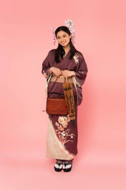 Japanese woman in kimono holding umbrella and handbag on pink background clipart