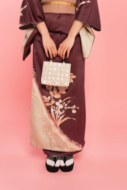 Cropped view of woman in oriental clothes holding handbag on pink background clipart