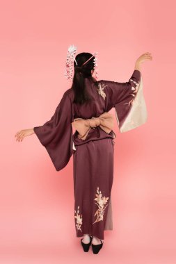 Kimono giymiş genç bir kadın ve pembe arka planda duran geleneksel saç stili.