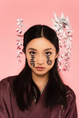 Yüzünde pembe izole edilmiş geleneksel saç şekli ve hiyeroglifleri olan güzel Japon kadın. 