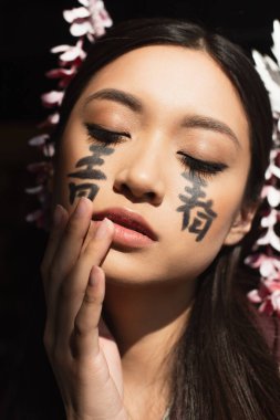 Yüzünde hiyeroglifler olan Japon kadın. Kapalı gözlerle siyahların üzerinde duruyor. 