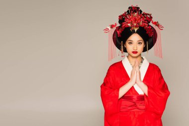 Asian woman with red lips showing praying hands isolated on grey  clipart