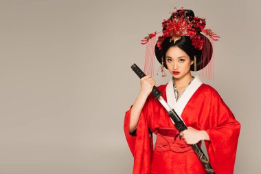 Japanese woman looking at camera and holding sword isolated on grey  clipart