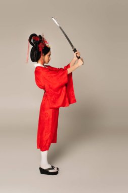Kırmızı elbiseli Japon kadının gri arka planda kılıca bakışı. 