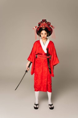 Kimonolu bir Japon kadının gri arka planda kılıç tutuşu. 