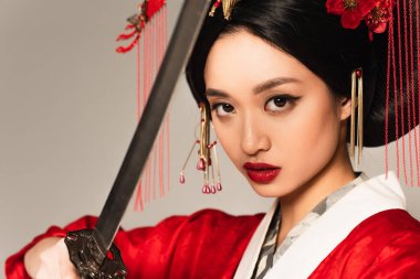 Kırmızı dudaklı Asyalı kadın, bulanık ön planda kılıcı tutuyor. Gri renkte izole edilmiş. 