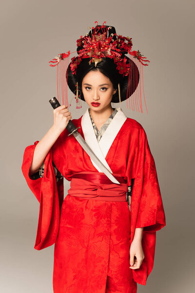 Asian woman holding sword and looking at camera isolated on grey 