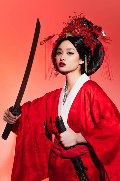 Japanese woman in oriental clothes holding sheath and sword on red background 
