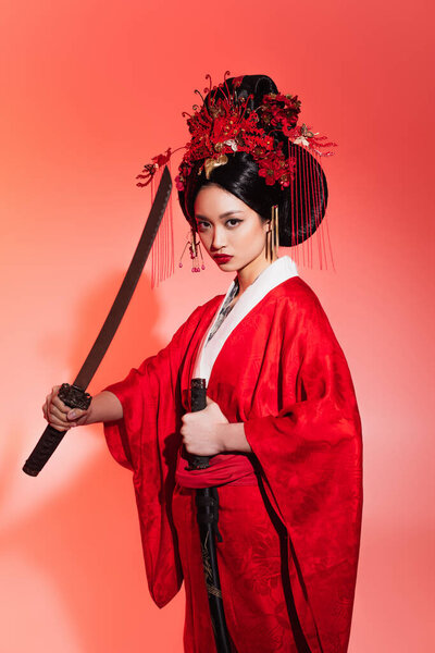 Japanese woman in authentic costume holding sheath and sword on red background 
