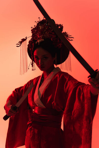 Asian woman with swords looking at camera on red background 