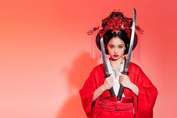 Asian woman in authentic kimono holding swords on red background 