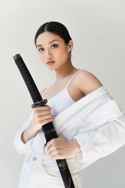 Young japanese woman holding sheath of sword isolated on grey