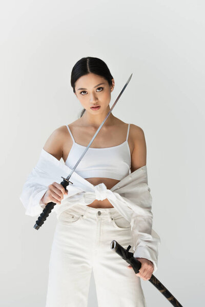 Young japanese woman with sheath and sword looking at camera isolated on grey