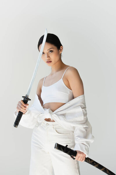 Pretty asian woman in white clothes holding sword isolated on grey
