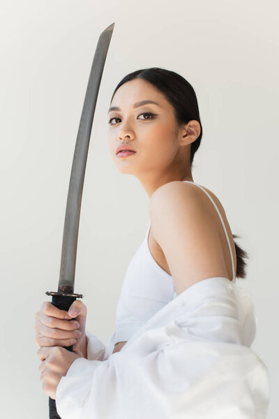 Low angle view of japanese woman with sword looking at camera isolated on grey
