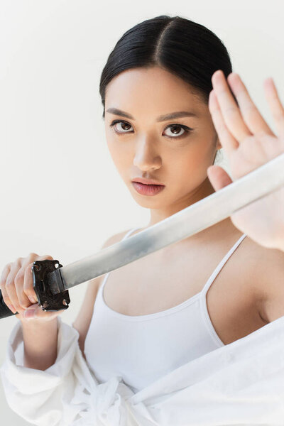 Young japanese woman touching sword on blurred foreground isolated on grey