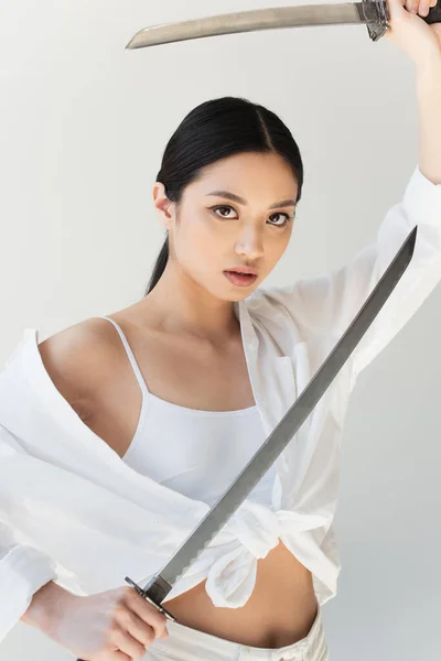白いシャツを着た若い日本人女性が灰色に孤立した刀を持っている — ストック写真