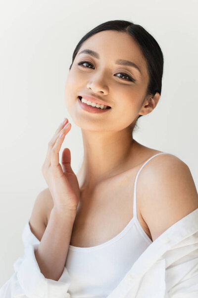 Portrait of happy asian woman in white shirt and top looking at camera isolated on grey