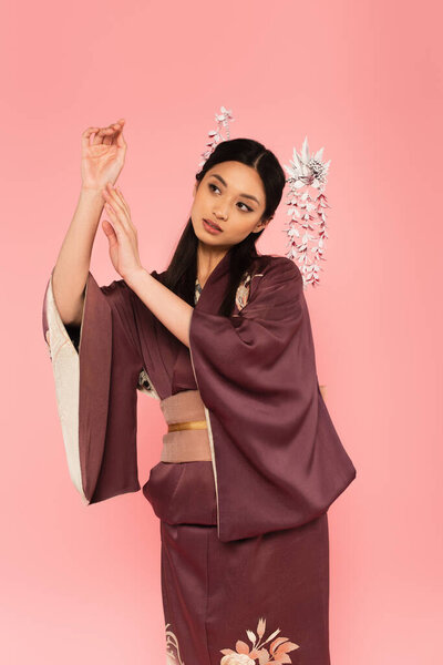 Японская женщина в традиционной одежде и прическе позирует на розовом 