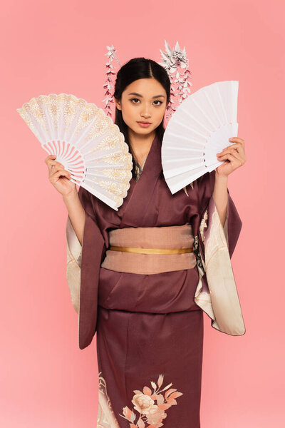Japanese woman in kimono posing with fans isolated on pink 