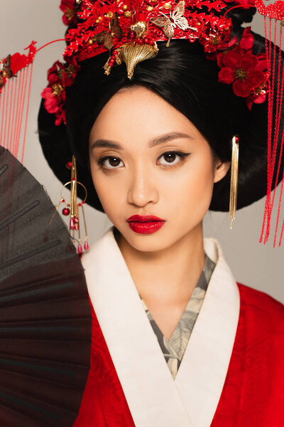 Asian woman with red lips holding black fan isolated on grey 