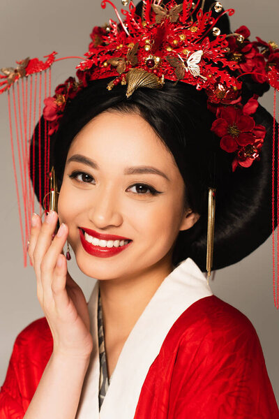 Cheerful asian woman with red lips looking at camera isolated on grey 