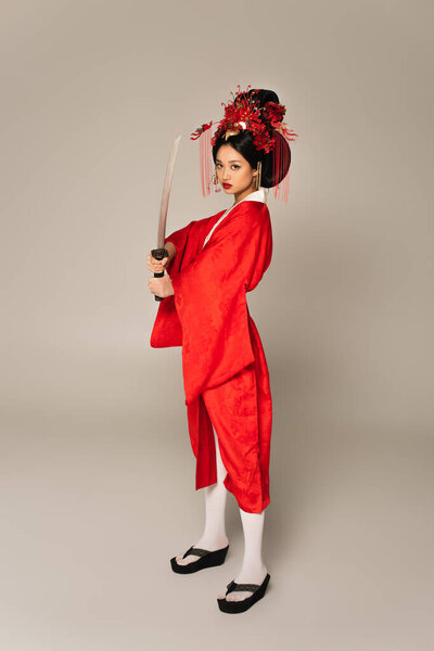 Full length of asian woman holding sword on grey background 