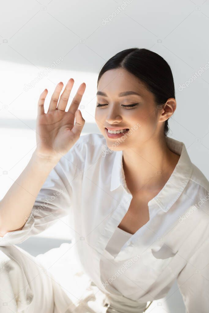 Smiling asian woman in white clothes sitting with closed eyes on grey background 