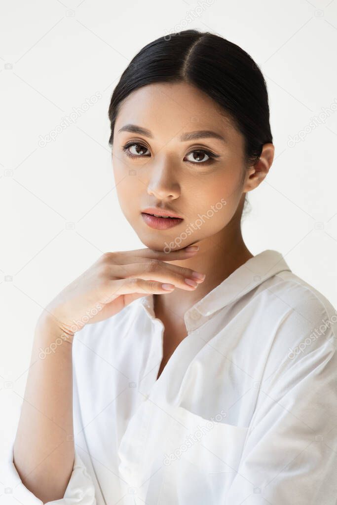 Young asian woman holding hand near chin isolated on grey