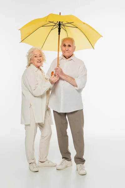 Glückliches Älteres Ehepaar Steht Mit Gelbem Regenschirm Auf Weißem Grund — Stockfoto