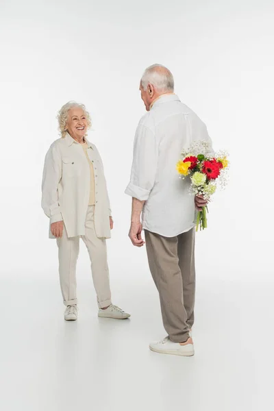 Anciano Escondiendo Ramo Flores Detrás Espalda Cerca Esposa Sonriente Blanco —  Fotos de Stock