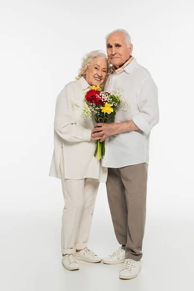 Happy Elderly Couple Hugging Holding Bouquet Flowers Looking Camera White — Stock Photo, Image