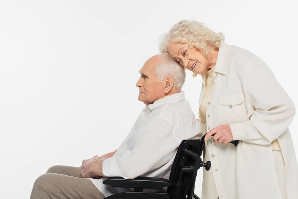 elderly woman gently touching husband in wheelchair with head isolated on white