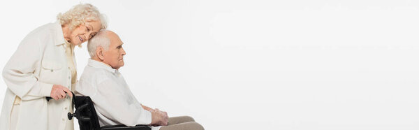 elderly woman gently touching husband in wheelchair with head isolated on white, banner