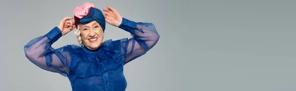 Sorrindo Mulher Idosa Vestido Azul Ajustando Turbante Com Mãos Isoladas — Fotografia de Stock