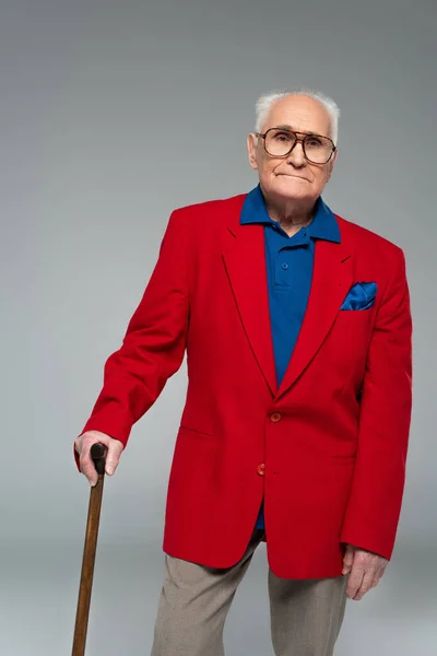 深刻な高齢者の男で赤のブレザーと眼鏡をかけて立ってグレーに隔離された — ストック写真