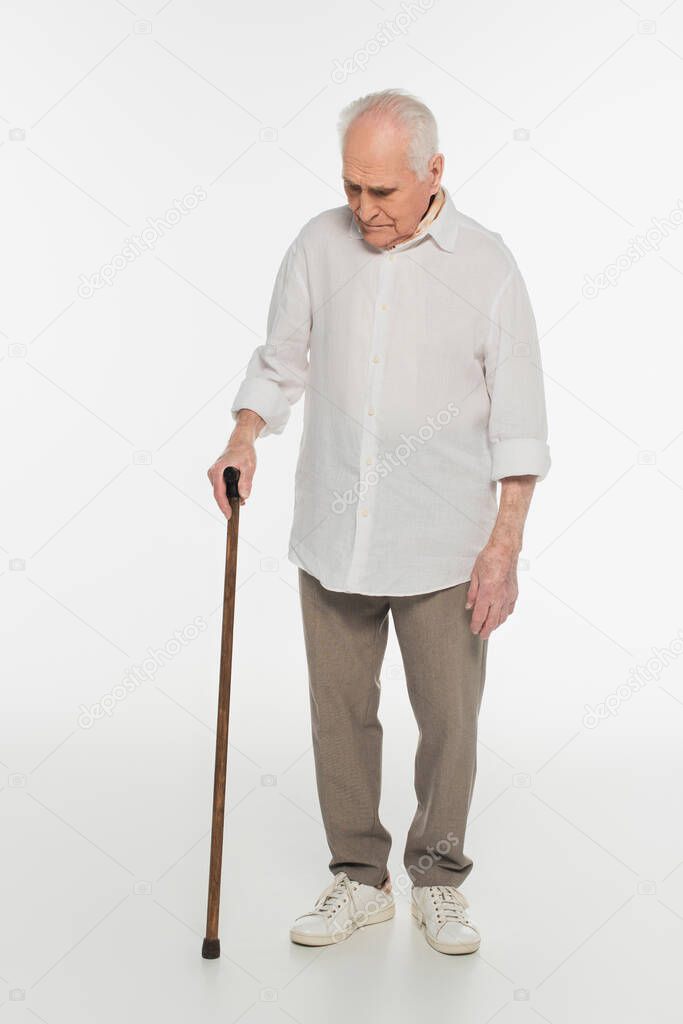 upset elderly man in casual clothes standing with walking stick on white