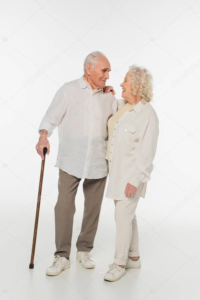 smiling elderly woman looking at husband with walking stick on white