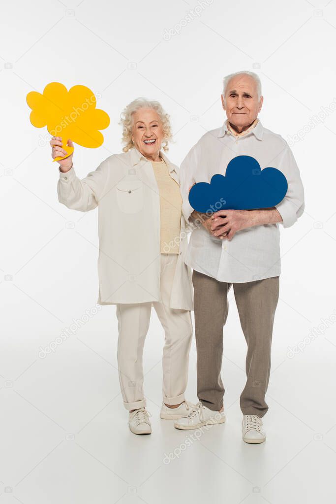 smiling elderly couple holding yellow thought bubbles and looking at camera on white