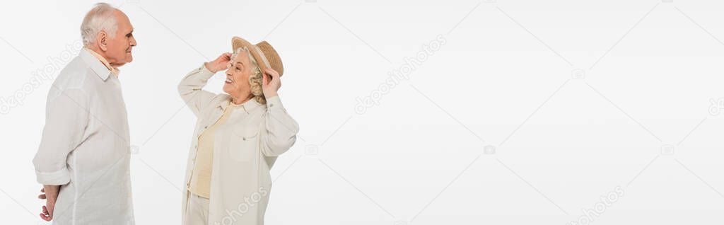 positive elderly woman adjusting hat on head and looking at husband, banner