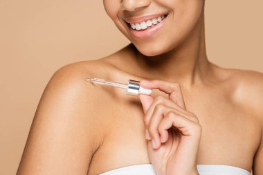 Çıplak omuzlarına serum takan, bej rengi izole edilmiş, mutlu, Afro-Amerikan kadın manzarası. 