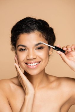 Mutlu Afro-Amerikalı kadın çıplak omuzlu kaşlarını bej rengi bir kaş ile izole etmiş. 
