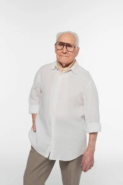 身穿休闲装 戴着眼镜 面带微笑的老人 手插在口袋里 望着被白色隔离的相机 — 图库照片