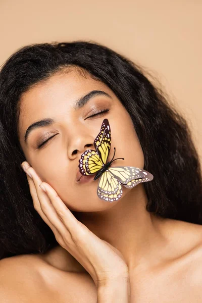 african american young woman with butterfly on lips and closed eyes isolated on beige