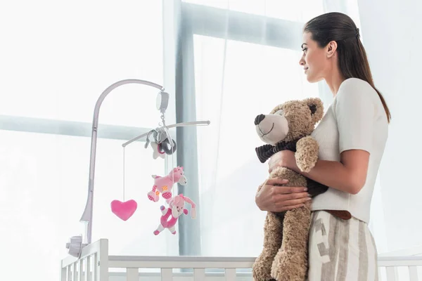 Vista Lateral Mujer Sosteniendo Oso Peluche Cerca Cama Bebé Casa — Foto de Stock