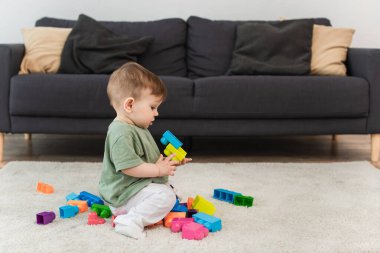 Halıda yapı taşı oynayan küçük çocuğun yan görünüşü 