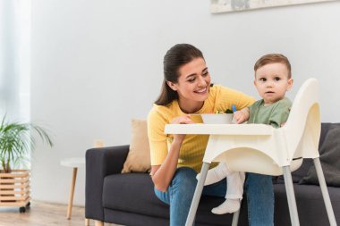 Mutlu anne, yüksek sandalyedeki yemek yanındaki çocuğa bakıyor. 